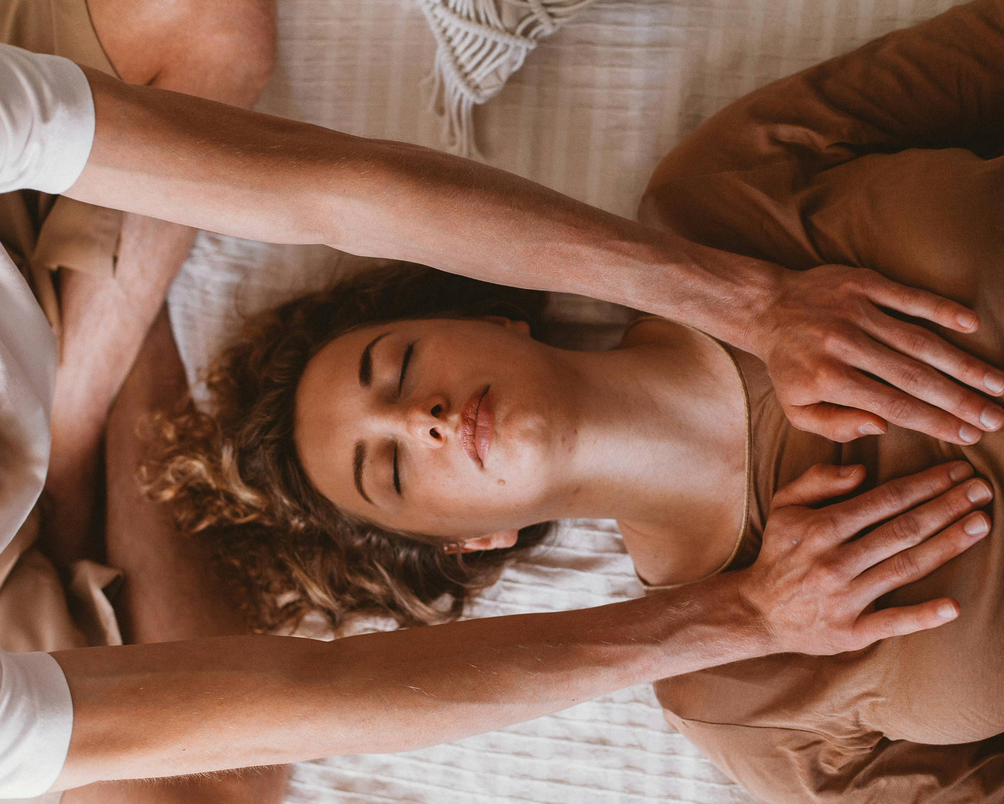 A woman lying peacefully as another person’s hands hover over her chest in a healing session, symbolizing energy work and upper chakra activation.