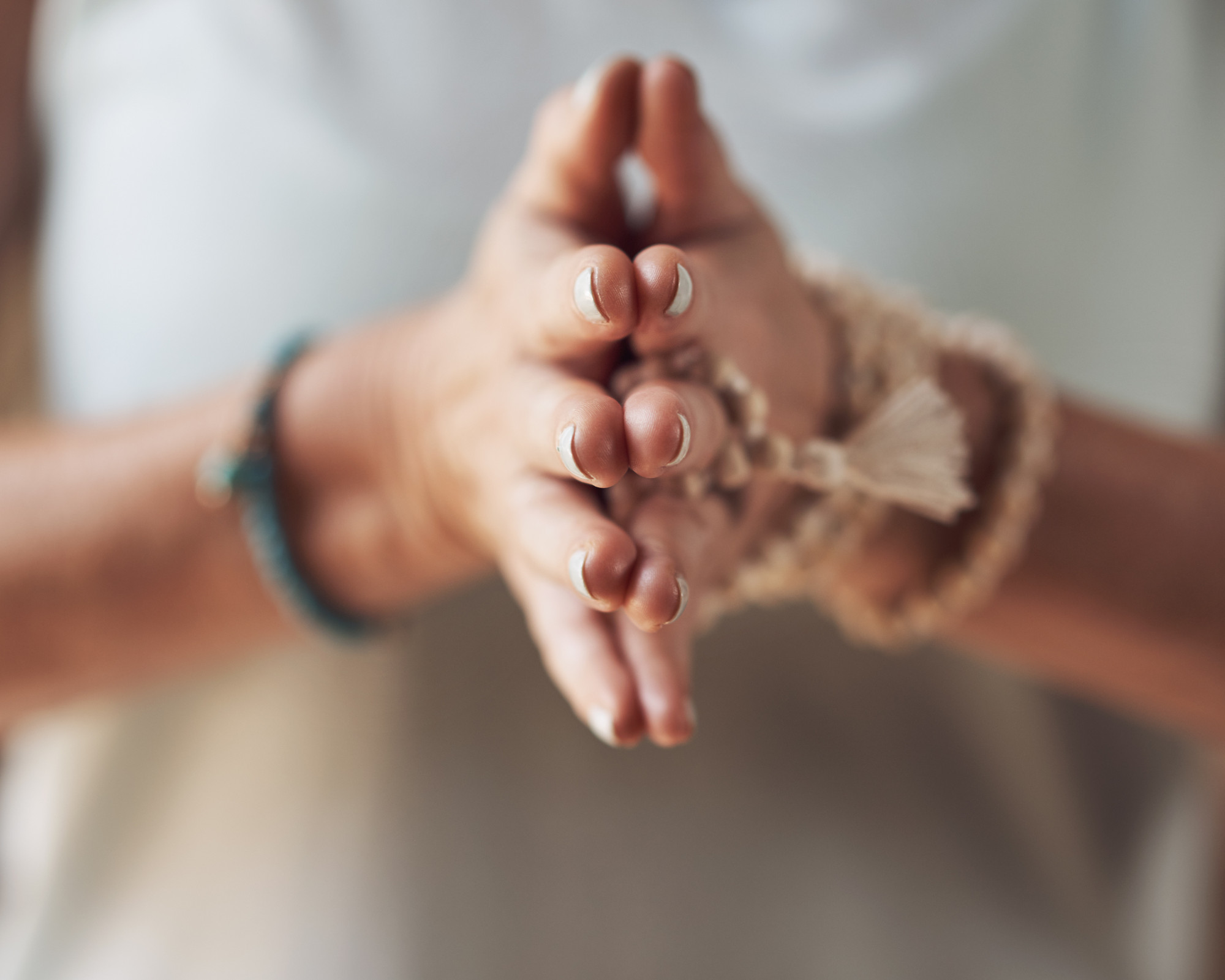 Close-up of a person’s hands in a prayer or grounding gesture, wearing spiritual mala bracelets, symbolizing mindfulness and Earth Star Chakra connection.