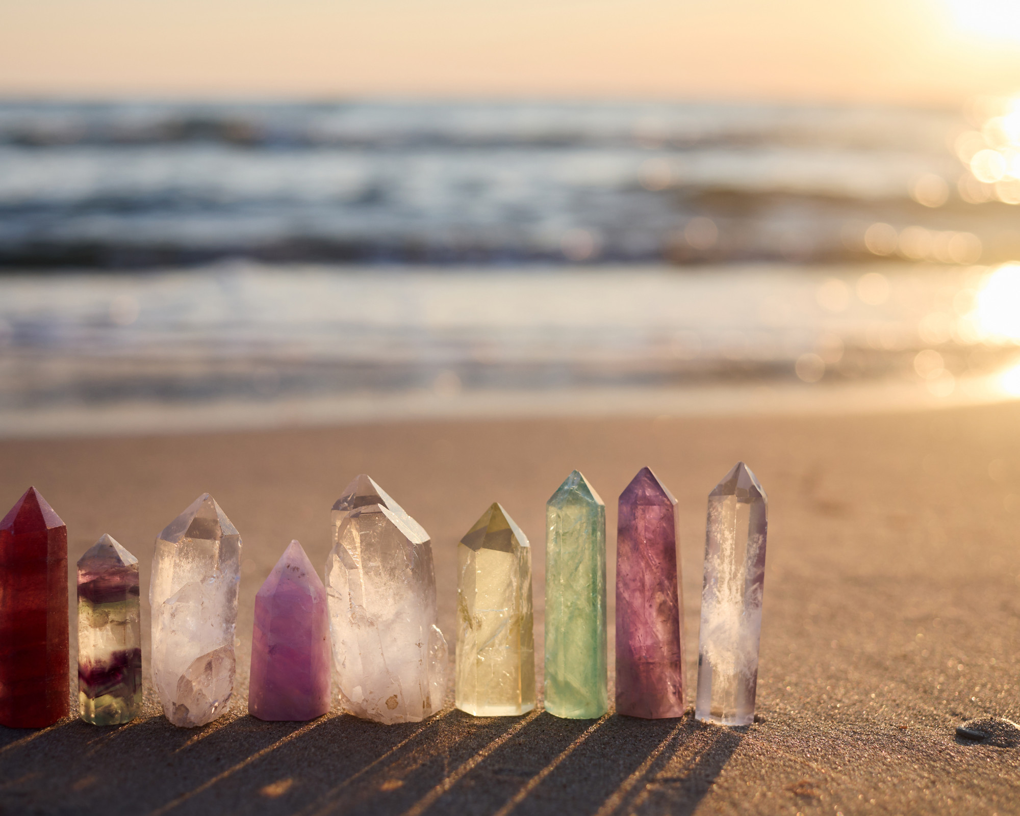 A row of healing crystals standing in the sand at sunset, symbolizing grounding energy and Root Chakra healing through first chakra stones and nature.