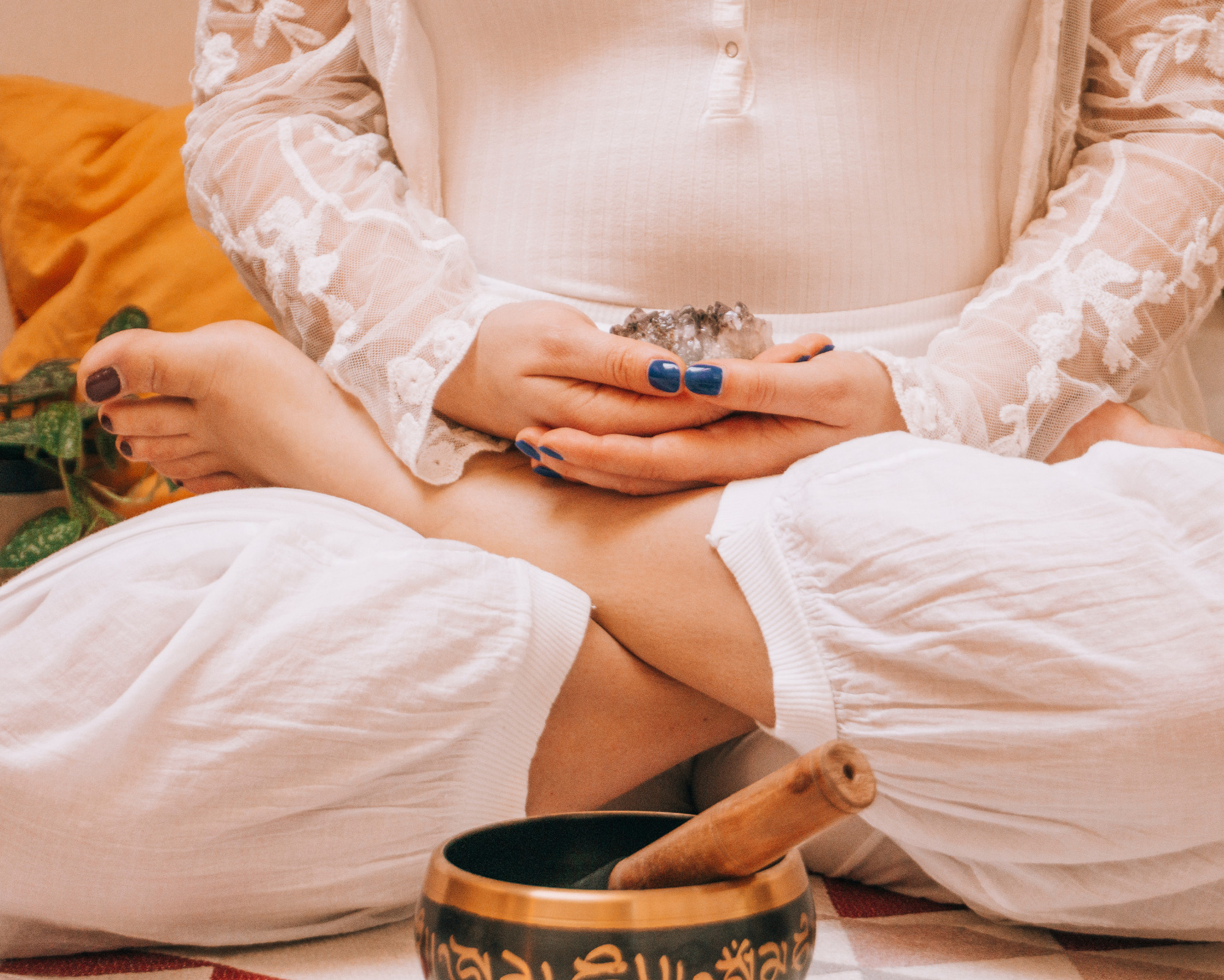 Woman sitting cross-legged in meditation, holding a crystal near the lower abdomen to support Sacral Chakra healing and emotional balance.