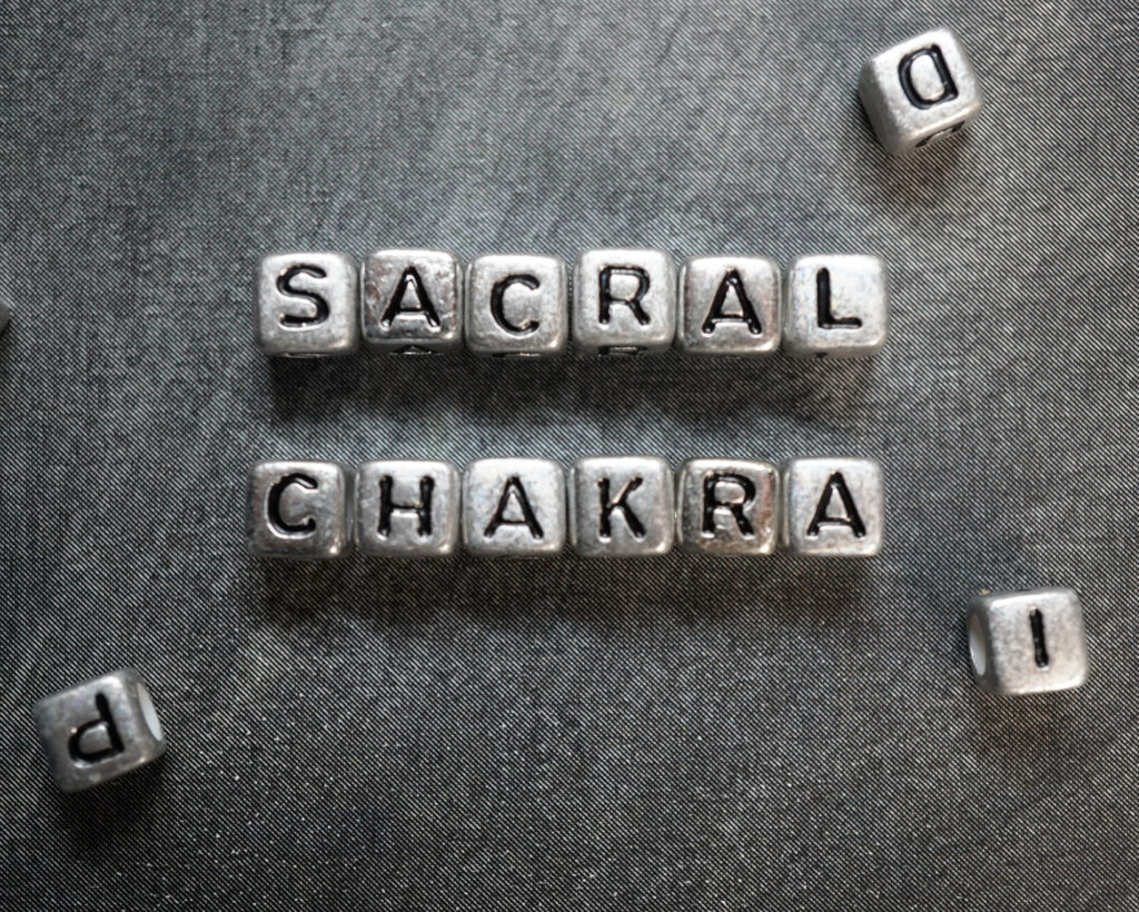Metal bead letters spelling “Sacral Chakra” on a textured gray background, symbolizing the second energy center in spiritual healing.