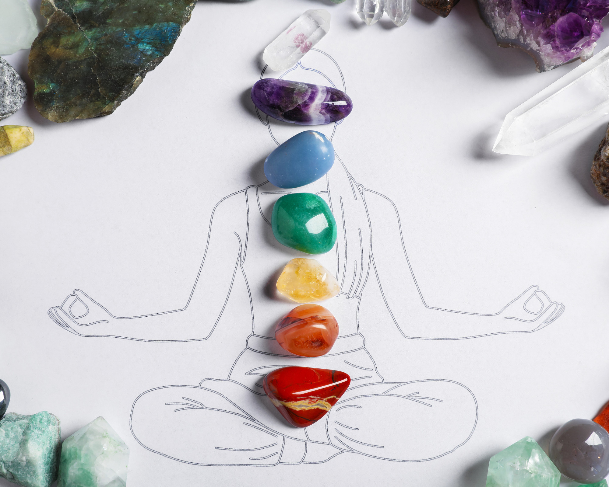 Colorful chakra stones placed along a sketch of a meditating person surrounded by healing crystals.