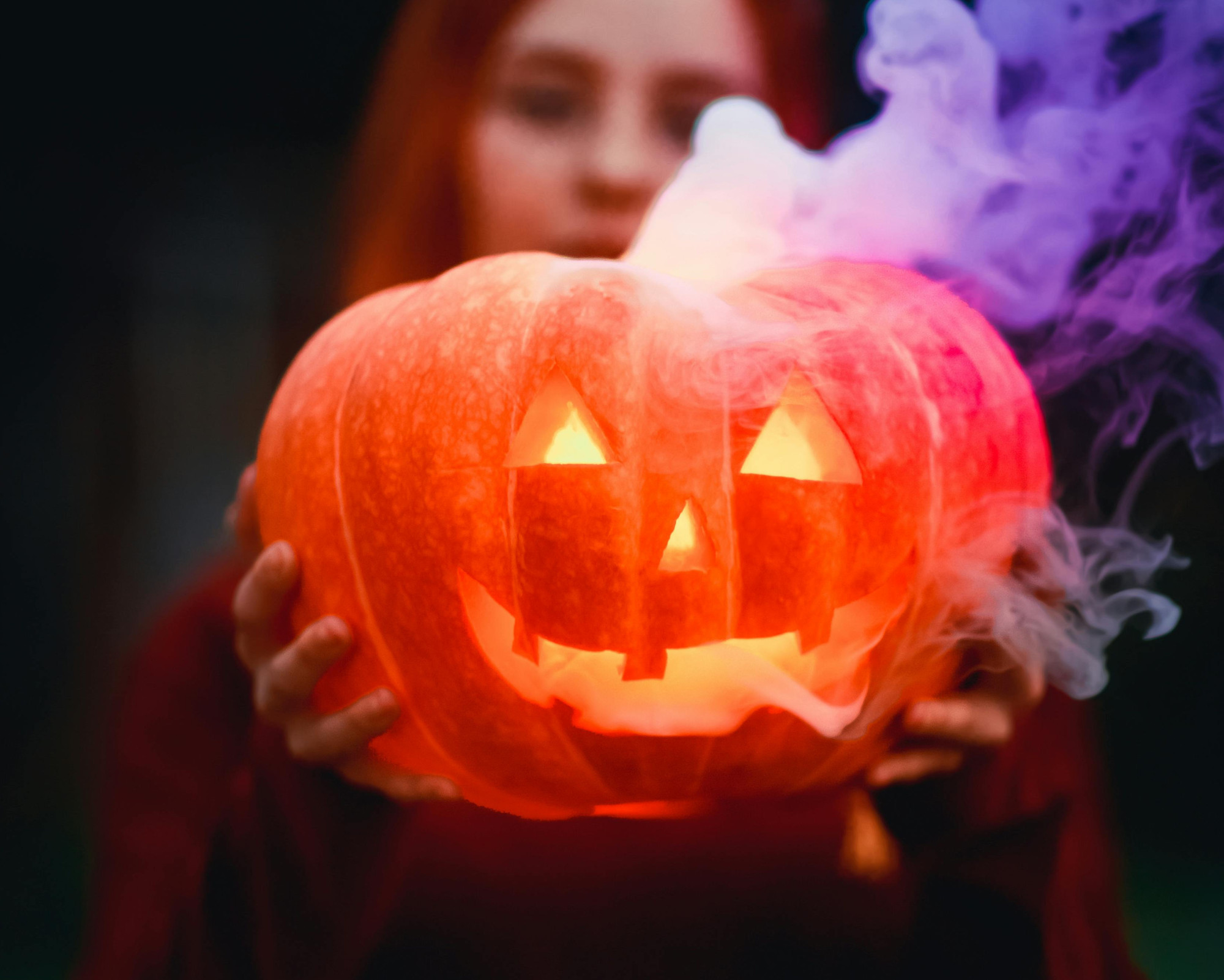 A woman holding a smoking jack-o’-lantern, illustrating what to do for Samhain through protective symbolism and seasonal rituals.