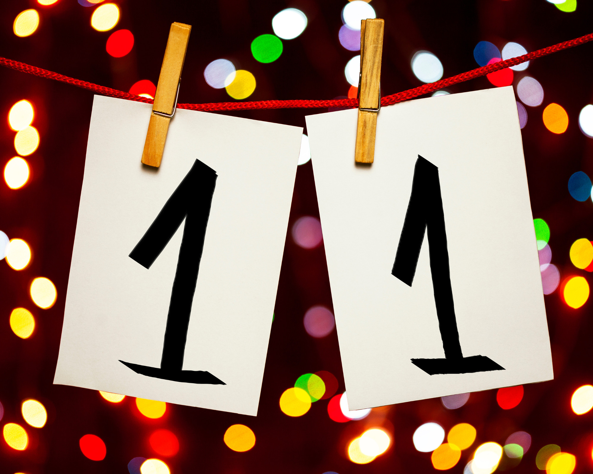 Creative representation of angel number 11 using two cards with the number 1 hanging on a string against colorful bokeh lights.