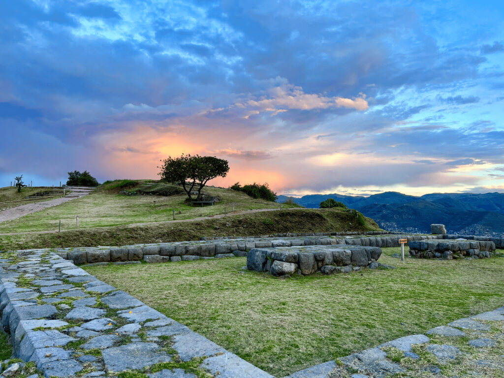 When the Mountains Called Me Home: How Peru Re-Mapped My Inner Compass Stone terraces and ruins of Sacsayhuamán overlooking Cusco at sunset with colorful clouds over the Andes.