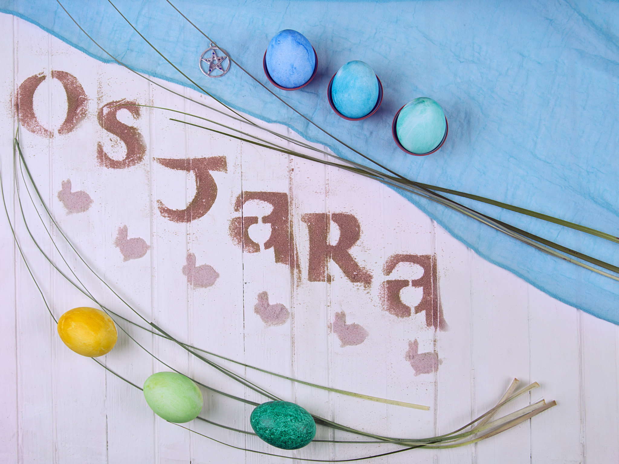Ostara easter flat lay with painted eggs, pentacle charm, and spring greenery arranged on wooden background.