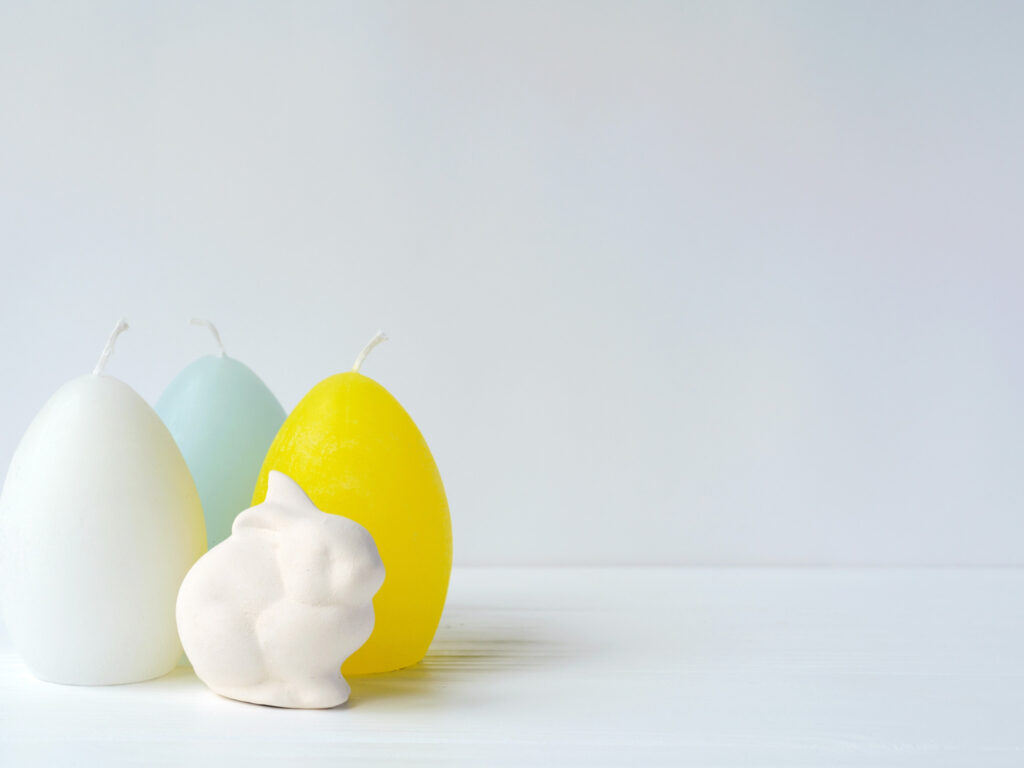 Minimal pastel egg candles and white bunny figure symbolizing ostara easter rebirth and spring equinox renewal.