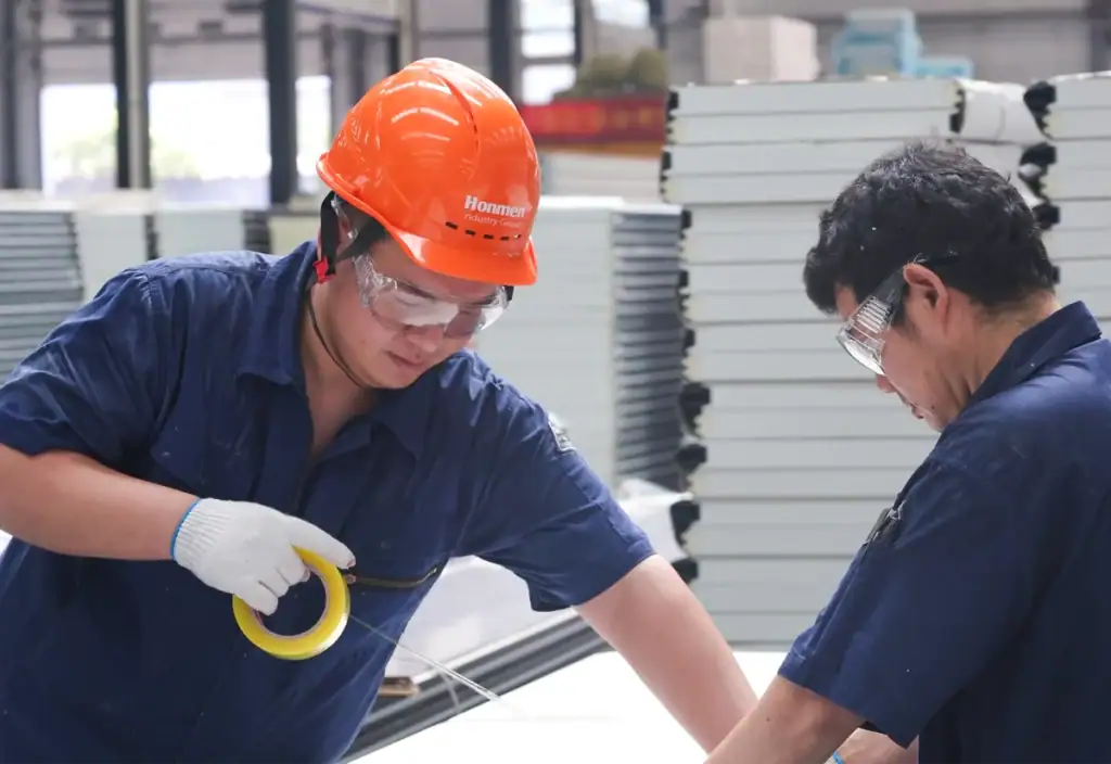Two workers measuring a door panel at a HONMEN Group manufacturing facility