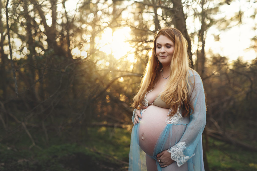 Pregnant Mama wearing sheer blue gown with sunset behind tree