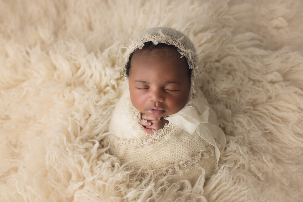 newborn baby girl in white fur wrapped in white in praying position