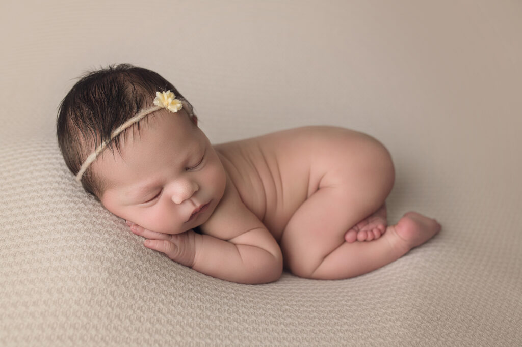 Newborn baby girl bum up on cream blanket