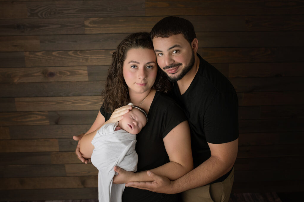 newborn baby girl in white wrapped being snuggled by parents