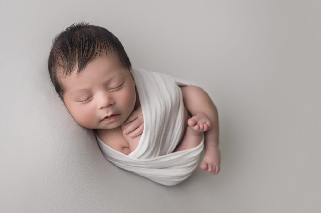 Newborn baby boy wrapped in white wrap laying on white blanket