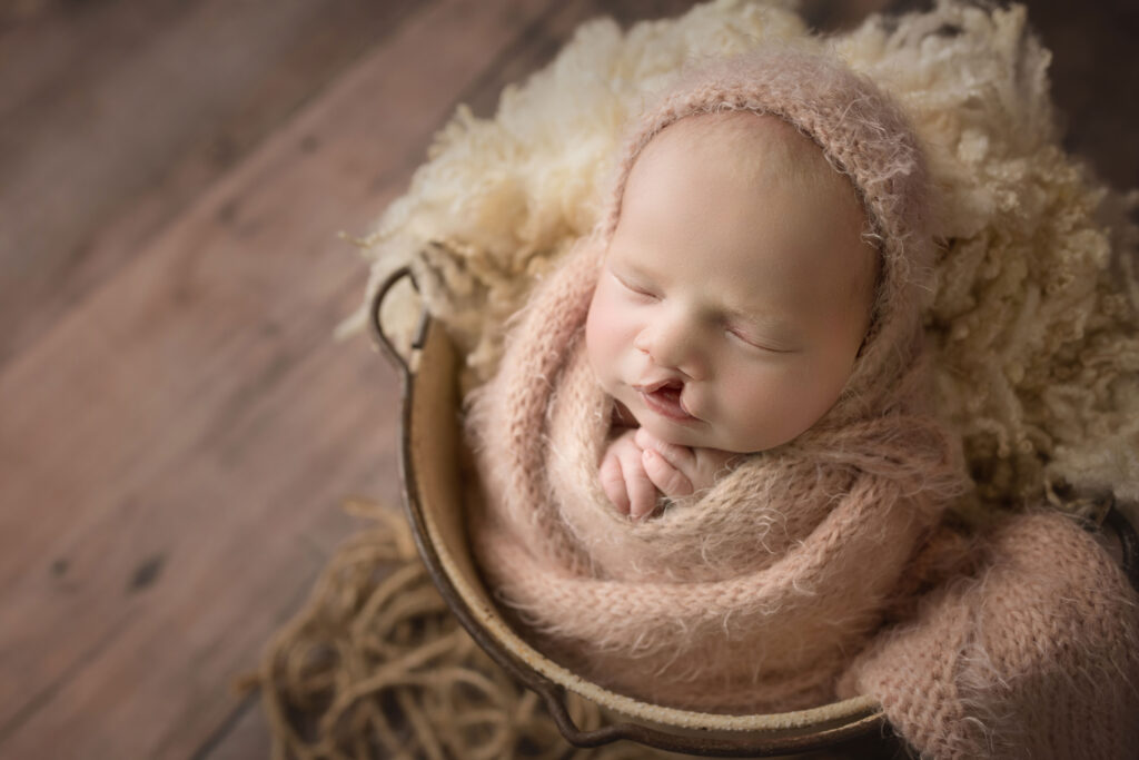 newborn baby girl wrapped in pink on pink fur