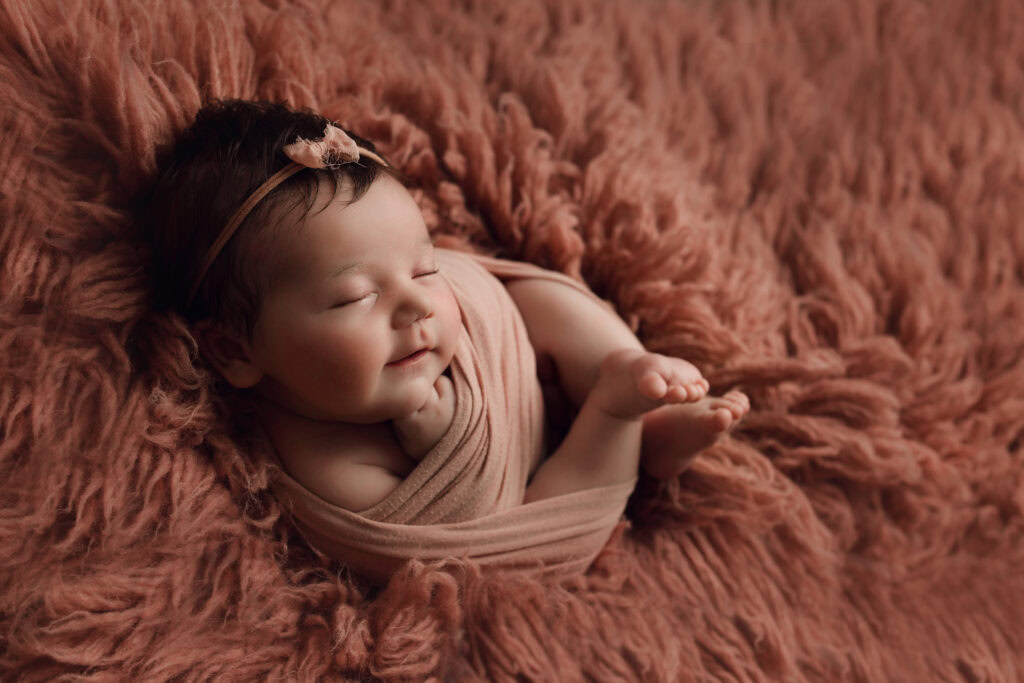 Newborn baby sleeping on textured pink blanket, adorable newborn photography.