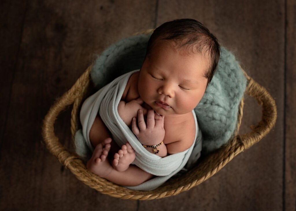 Sleeping baby boy wrapped in a blue swaddle, peacefully posed in a woved basket