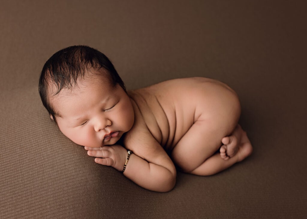 Sleeping newborn baby boy posed on his tummy with his hands tucked beneath his face