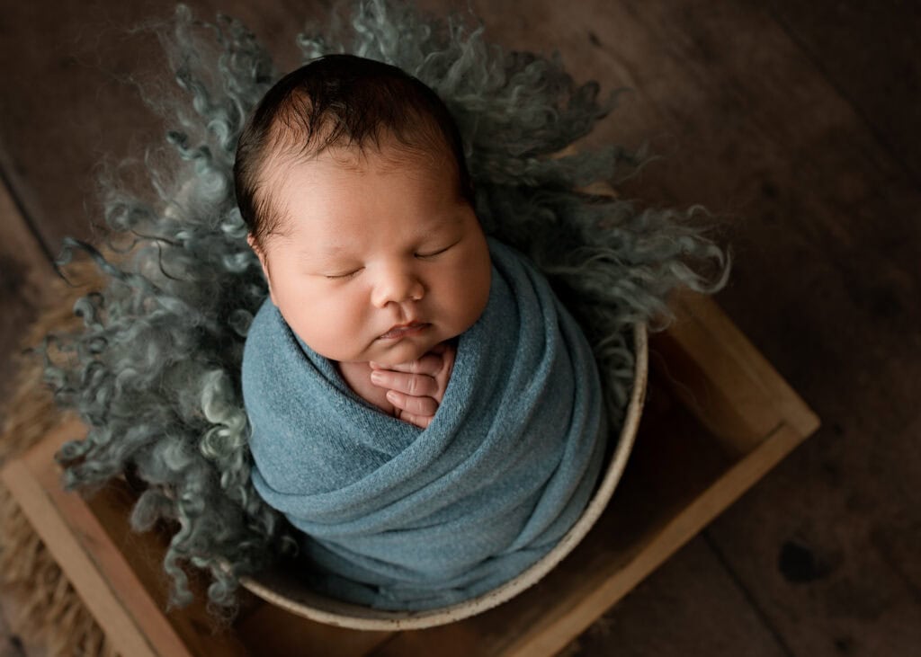 Newborn baby boy sleeping peacefully while wrapped in a soft blue blanket in a bucket