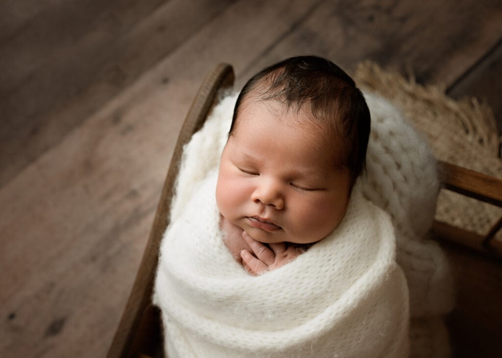 Newborn baby boy peacefully sleeping while wrapped in a soft cream blanket