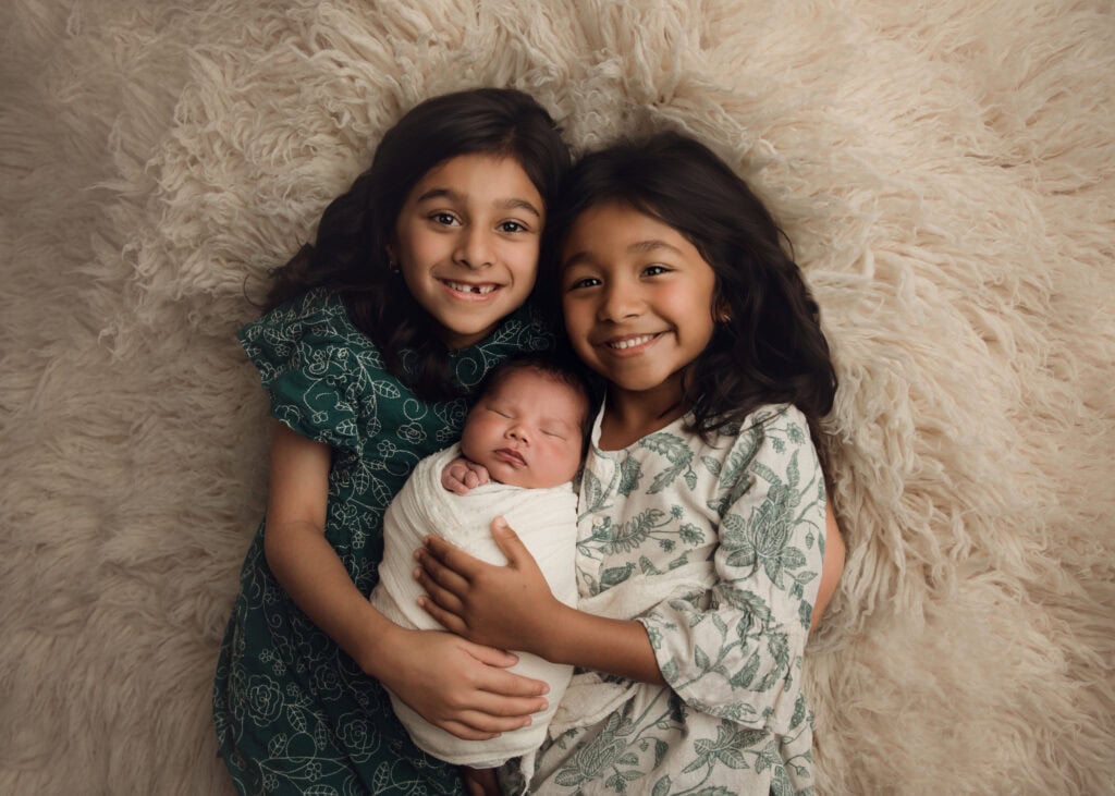 Newborn baby boy cuddled between his two older sisters during a newborn photography session