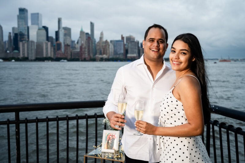 6 Surprise Proposal Tips to Prepare for the Big Engagement! Couple toasting champagne with city skyline view.