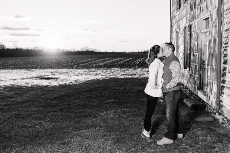 The Perfect Black & White Photo Editing Style Couple kissing by rustic house at sunset.