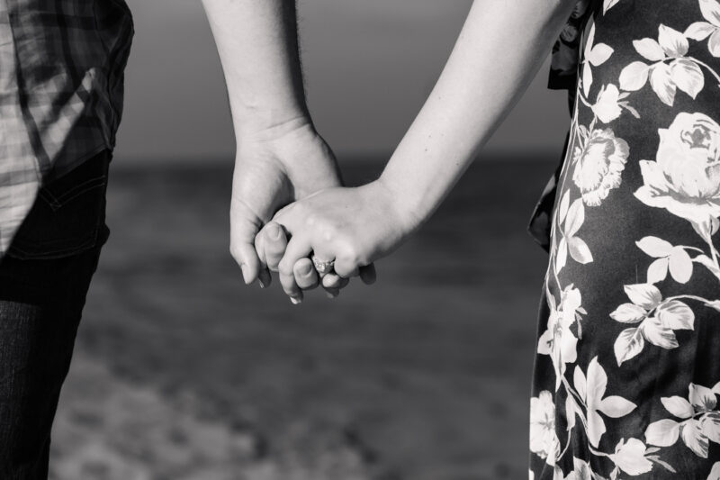 The Perfect Black & White Photo Editing Style Couple holding hands on the beach, engagement ring visible.