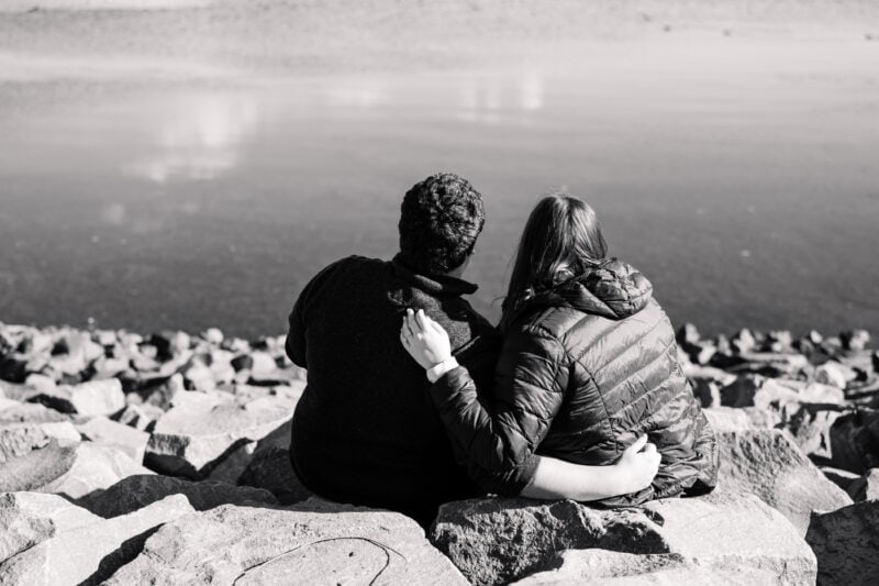 The Perfect Black & White Photo Editing Style Couple sitting on rocks by a lake.