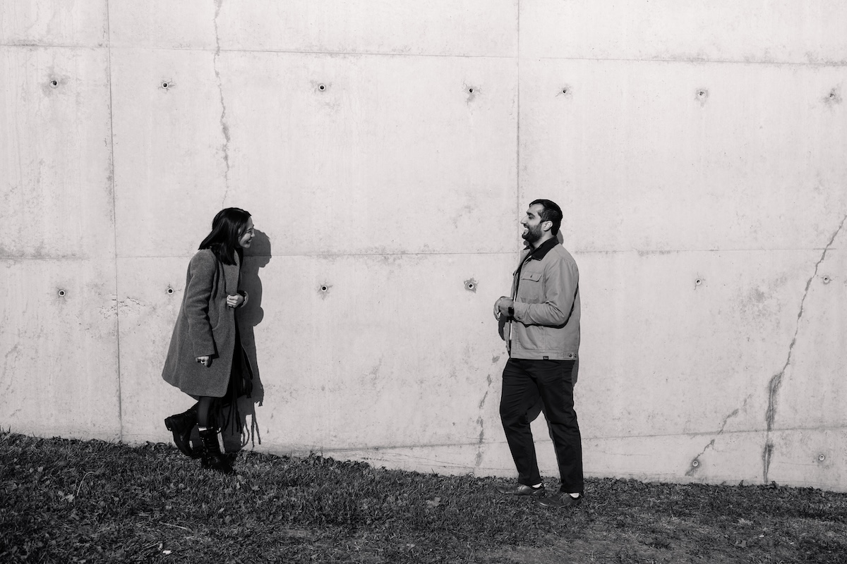 Two people talking outside against a concrete wall.
