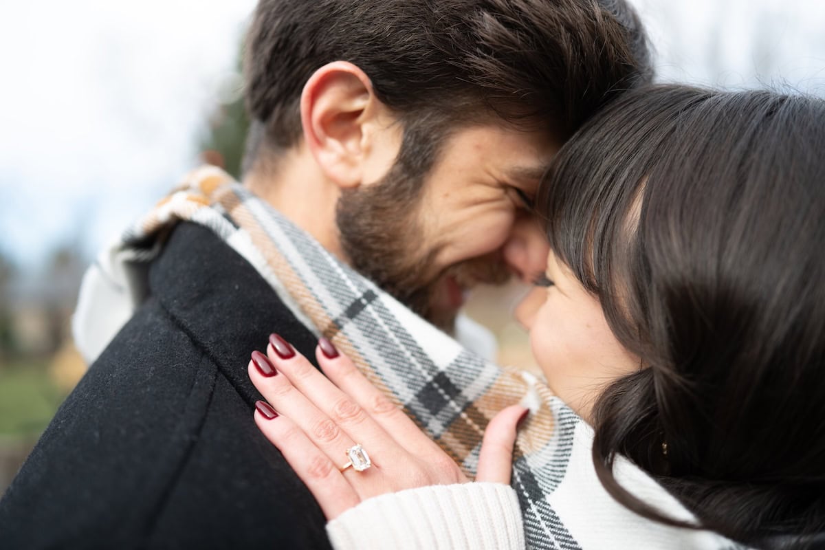 Couple embracing closely with engagement ring visible.