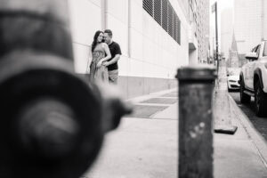 Couple embraces on urban sidewalk, black and white photo.