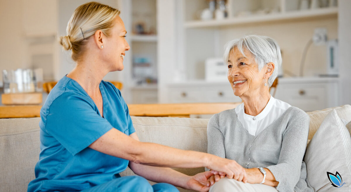 Caregiver sitting with senior woman on a couch reassuring her things will be ok