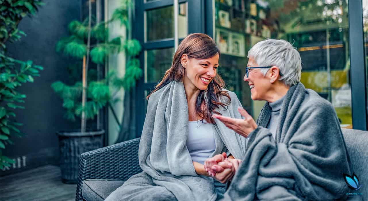Adult daughter discussing assisted living with her elderly mother on their couch at home