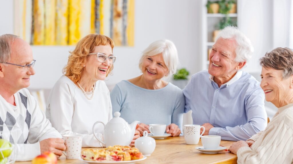 Group of seniors smiling at a table having tea and a nice conversation