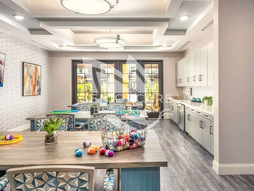 Craft room at Clearwater at Pinnacle Peak with work tables, patterned chairs, a basket of yarn, a kitchenette, and French doors to the courtyard.