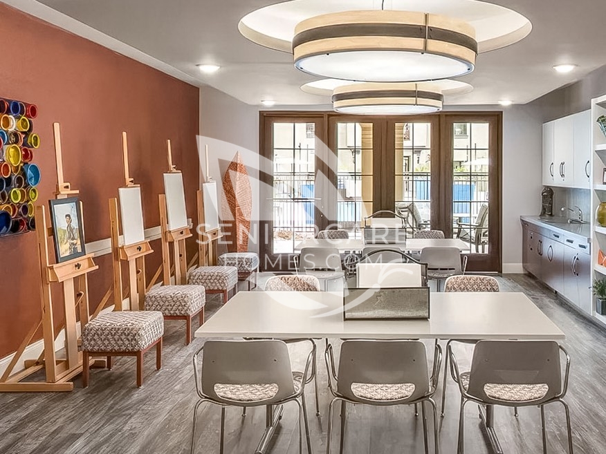 Art studio at Clearwater at Pinnacle Peak with a row of wooden easels, a terracotta accent wall, a large work table, and French doors.