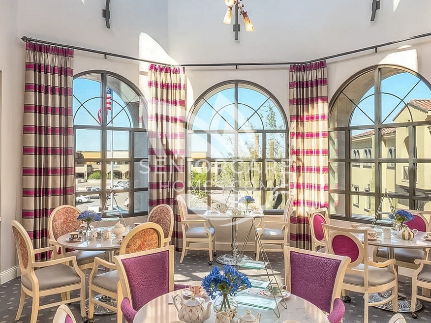 Tea room at Clearwater at Pinnacle Peak with round tables set for tea, magenta and cream chairs, striped drapes, and tall arched windows.