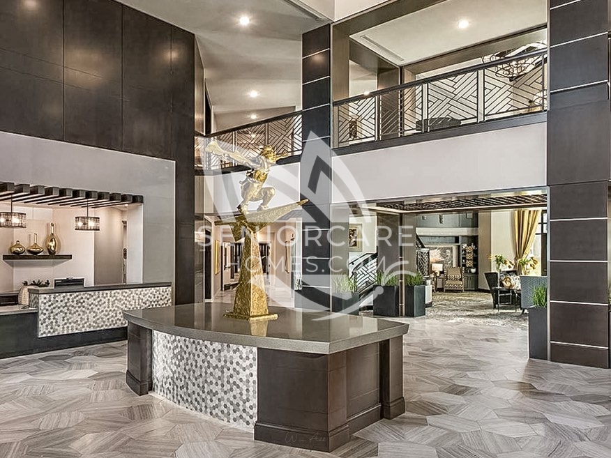 Two-story lobby at Clearwater at Pinnacle Peak with a gold sculpture centerpiece, hexagon-tiled floors, a concierge desk, and an upper-level balcony.