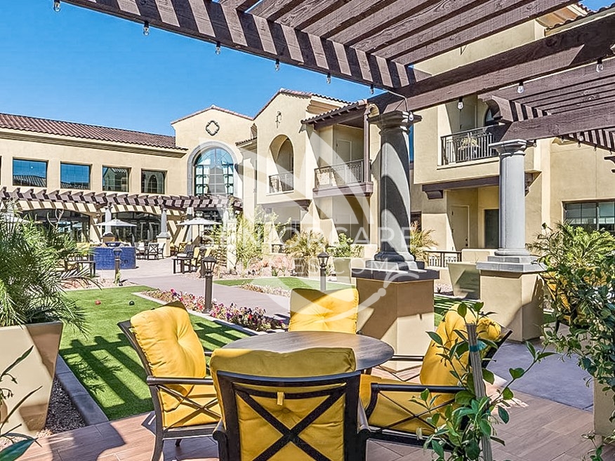 Courtyard at Clearwater at Pinnacle Peak with yellow-cushioned patio seating under a wooden pergola, a lawn area, and Mediterranean-style buildings.