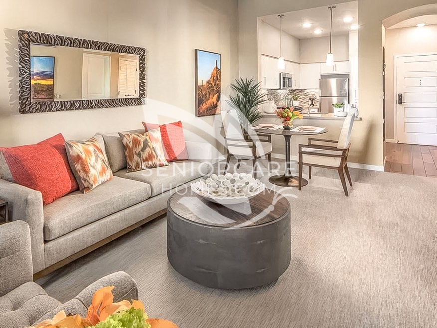 Furnished apartment at Clearwater at Pinnacle Peak with a neutral sofa, coral throw pillows, a round coffee table, a bistro table, and an open kitchen.