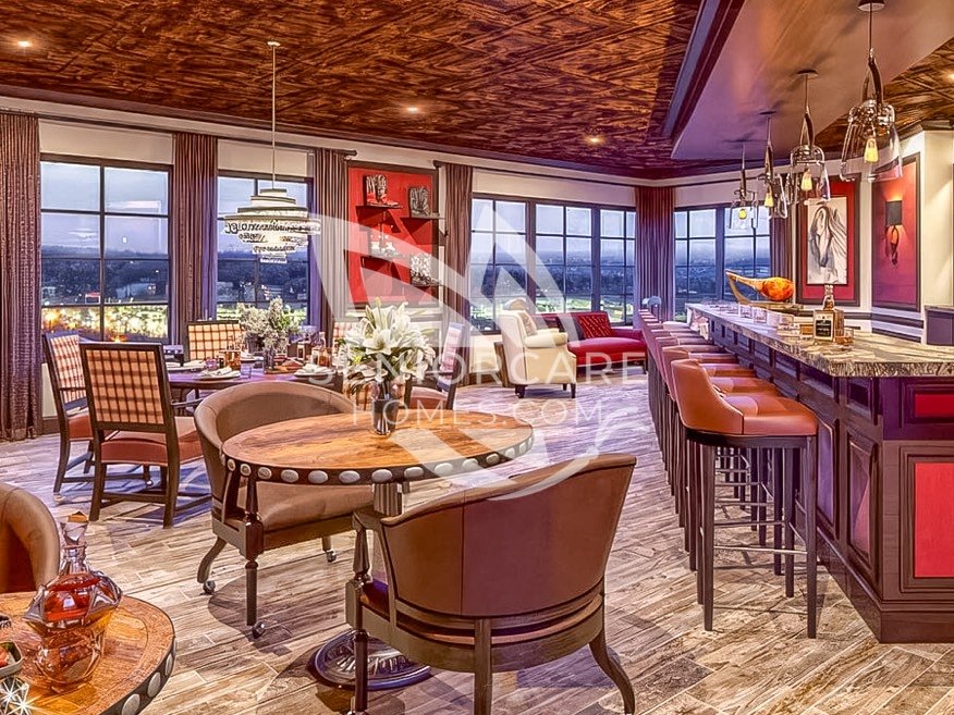 Lounge and bar at Clearwater at Pinnacle Peak with leather bar stools, round game tables, red accent walls, and large windows with evening views.