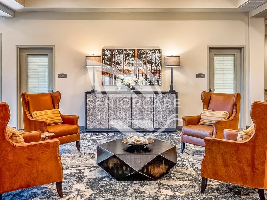 Lounge at Clearwater at Rancharrah with four rust-colored wingback chairs around a faceted black coffee table and a forest landscape painting.