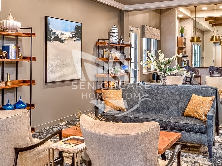 Sitting area at Clearwater at Rancharrah with a blue velvet sofa, gold accent pillows, cream armchairs, and open shelving with decor.