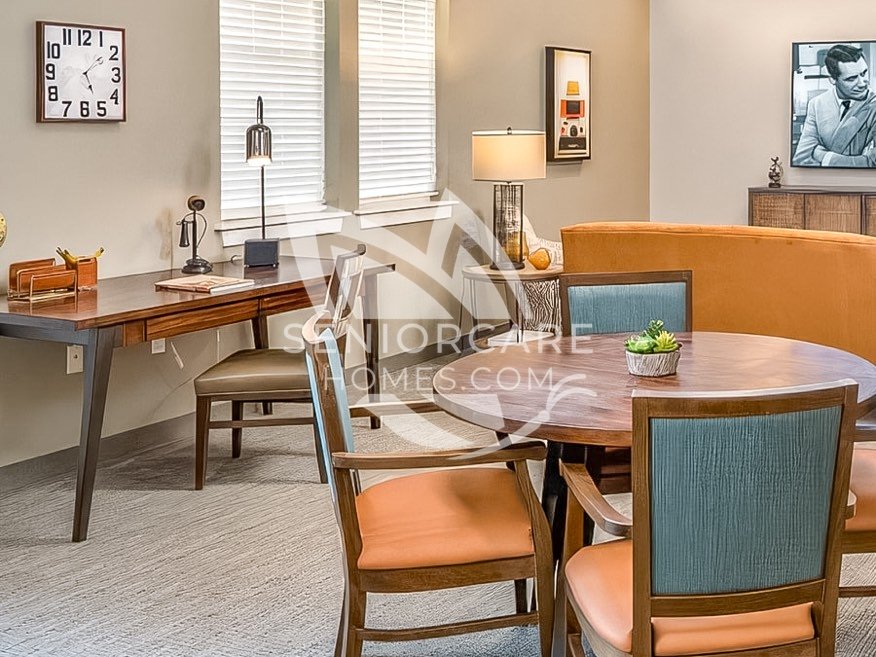 Activity room at Clearwater at Rancharrah with a writing desk, a round table with blue and orange chairs, retro decor, and a vintage black-and-white portrait.