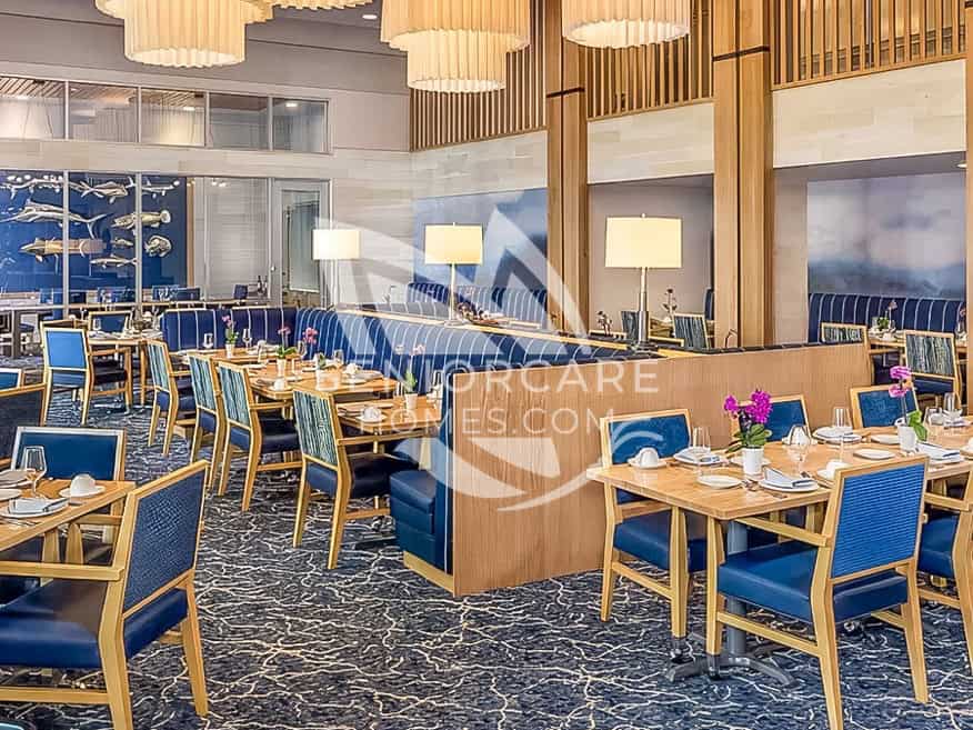 Main dining room at Clearwater at Riverpark with navy banquette seating, blue upholstered chairs, wood tables, and drum pendant lights.