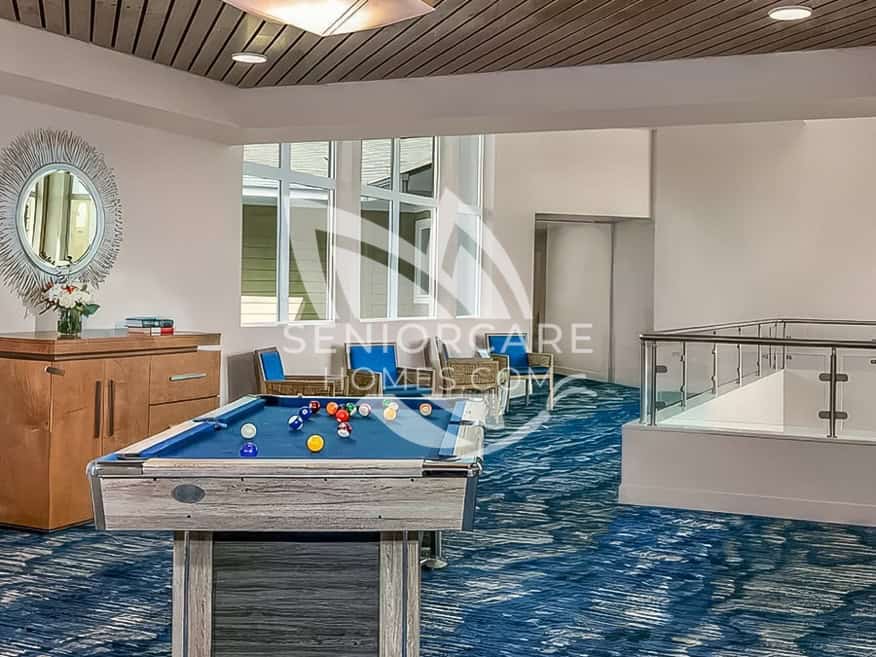 Game room at Clearwater at Riverpark with a pool table, blue accent chairs, a sunburst mirror, and ocean-blue patterned carpet.