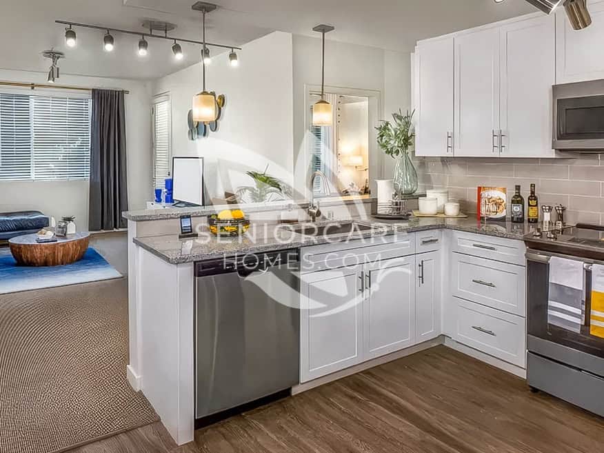 Apartment kitchen at Clearwater at Riverpark with white cabinets, granite countertops, stainless steel appliances, and an open view to the living room.
