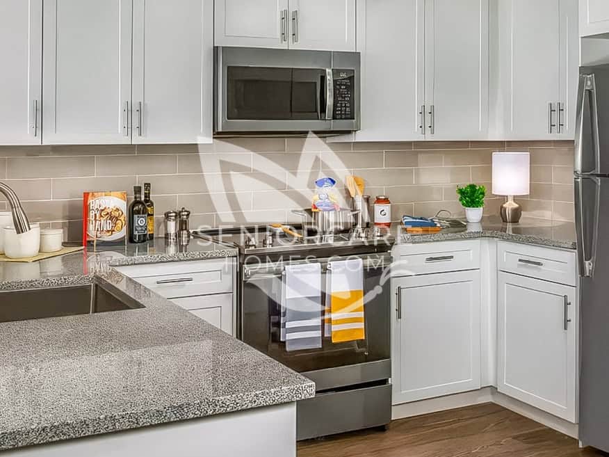 Close-up of an apartment kitchen at Clearwater at Riverpark with granite counters, a subway tile backsplash, and a stainless steel range and microwave.