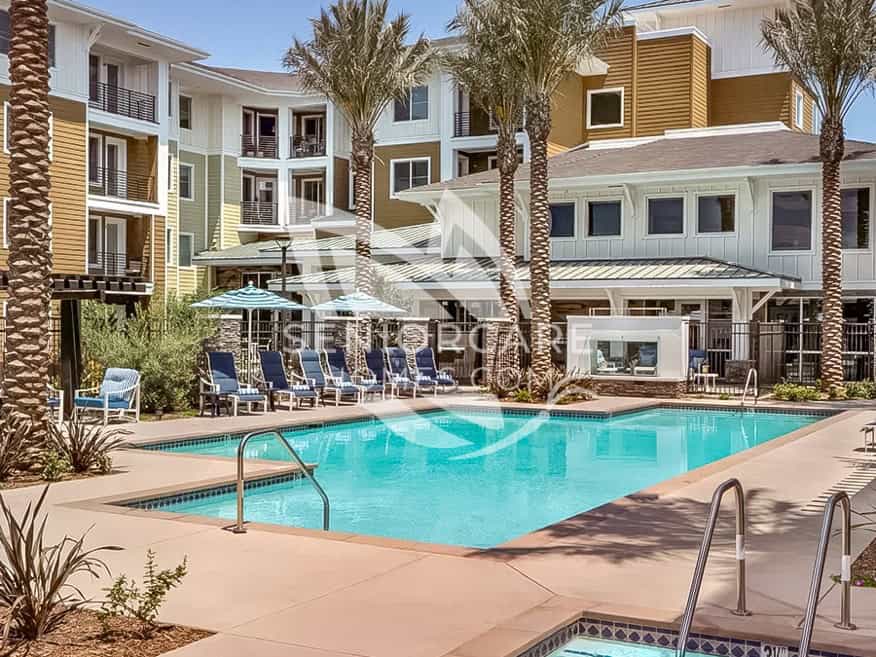 Resort-style pool at Clearwater at Riverpark with blue lounge chairs, striped umbrellas, palm trees, and a hot tub in front of the residential buildings.