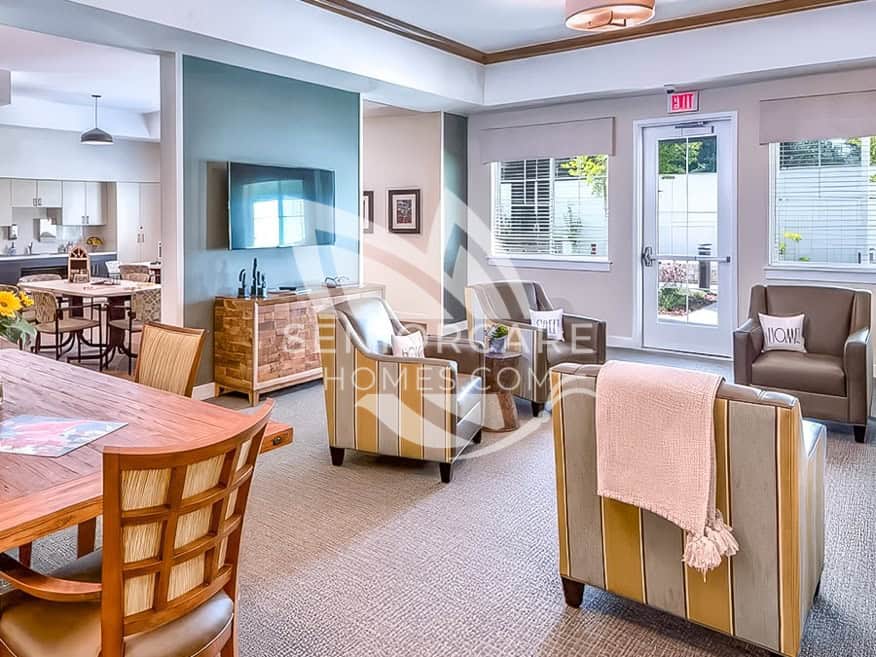 Common living room at Clearwater at Sonoma Hills with striped armchairs, a wall-mounted TV, a wooden dining table, and a door to the garden.